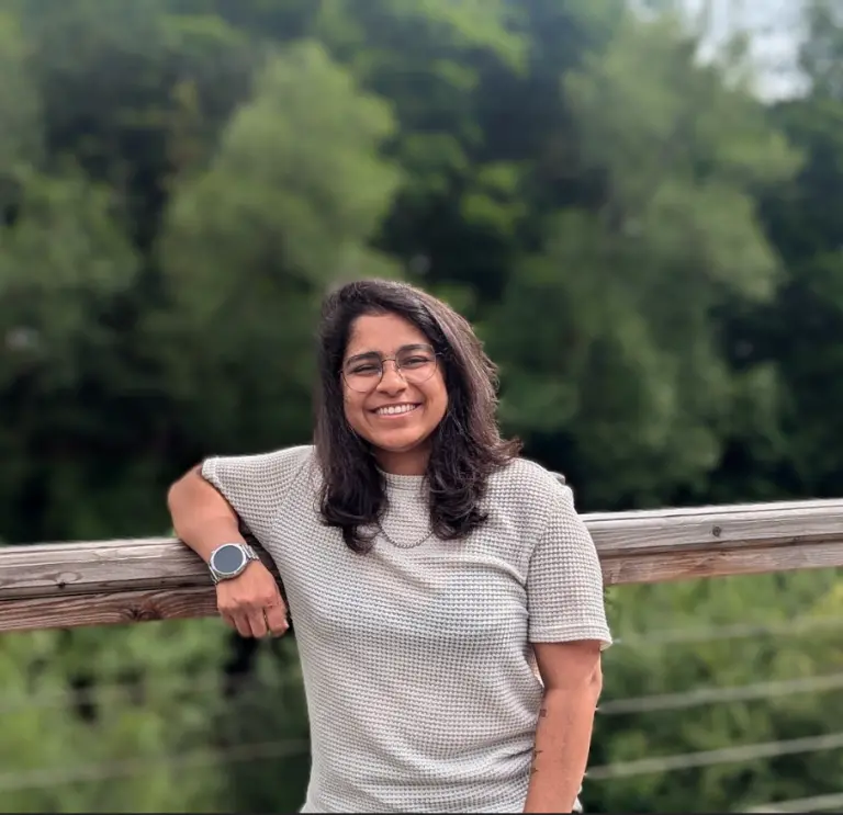 Woman leaning on fence with green foresty in background